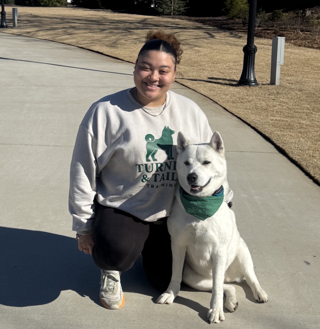 Alliyah Turner kneeling beside a white akita, both in Turner & Tails green